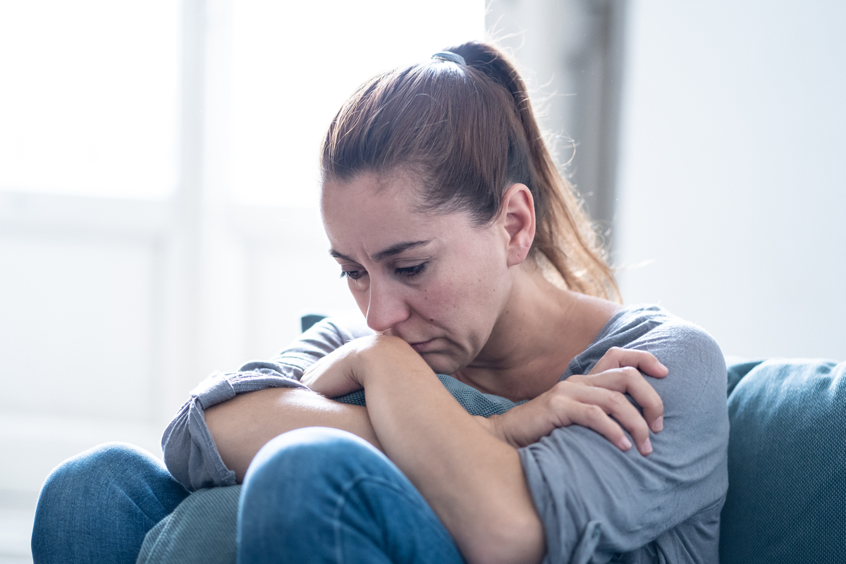 middle aged white woman sitting on floor resting arms on knees looking sad