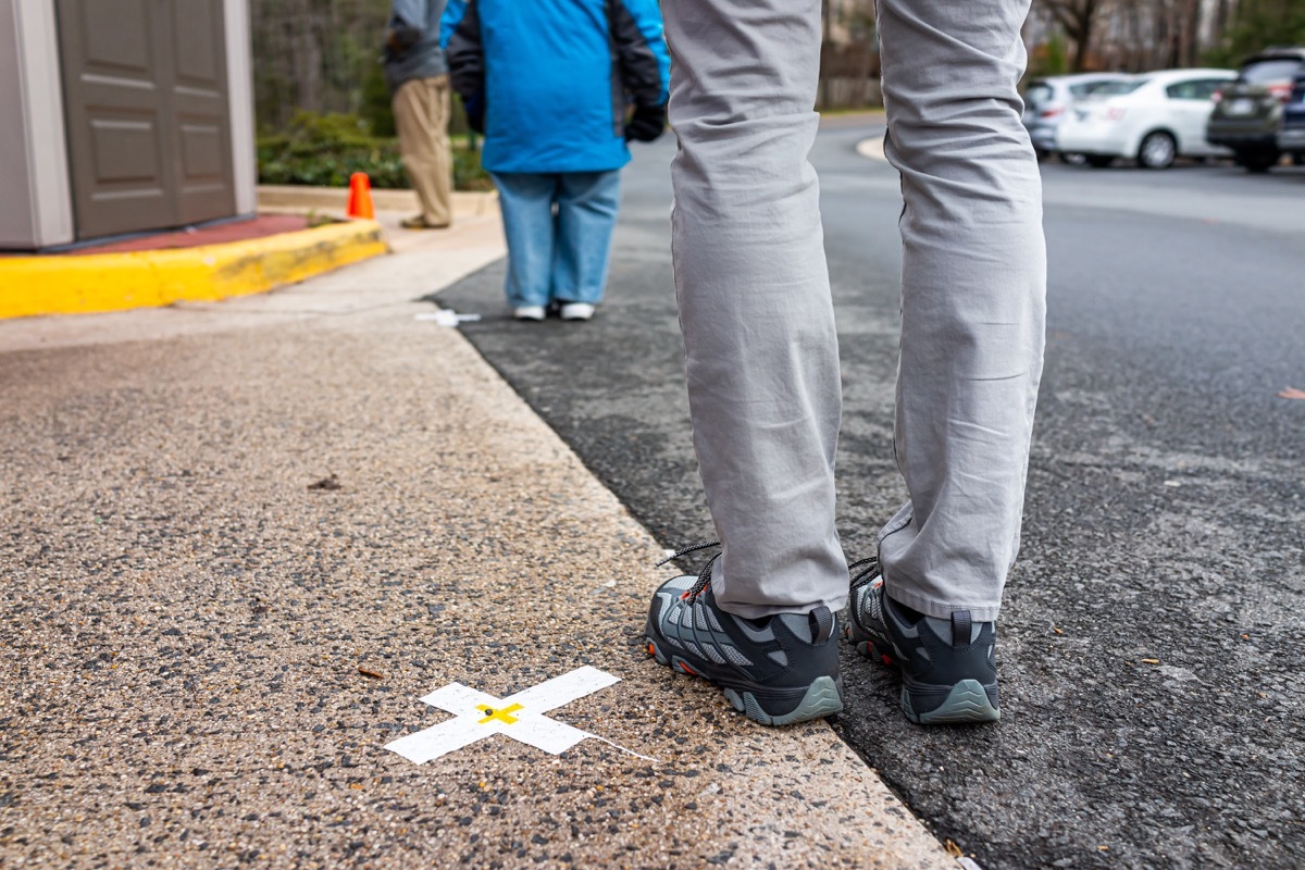 People standing waiting in line far apart to maintain social distance distancing during covid-19 coronavirus outbreak with mark cross signs on sidewalk pavement by grocery food store shop shopping