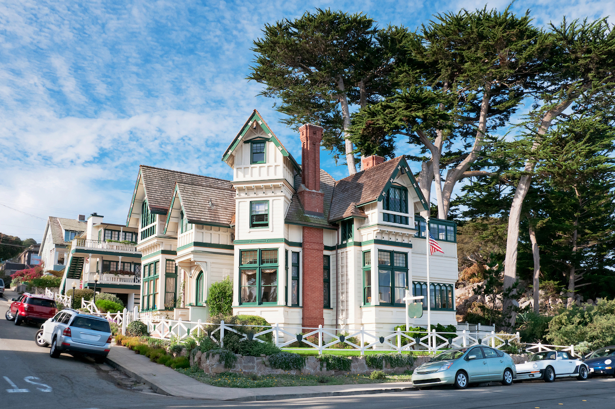 A large white Victorian house with green trim on a corner in Pacific Grove, California