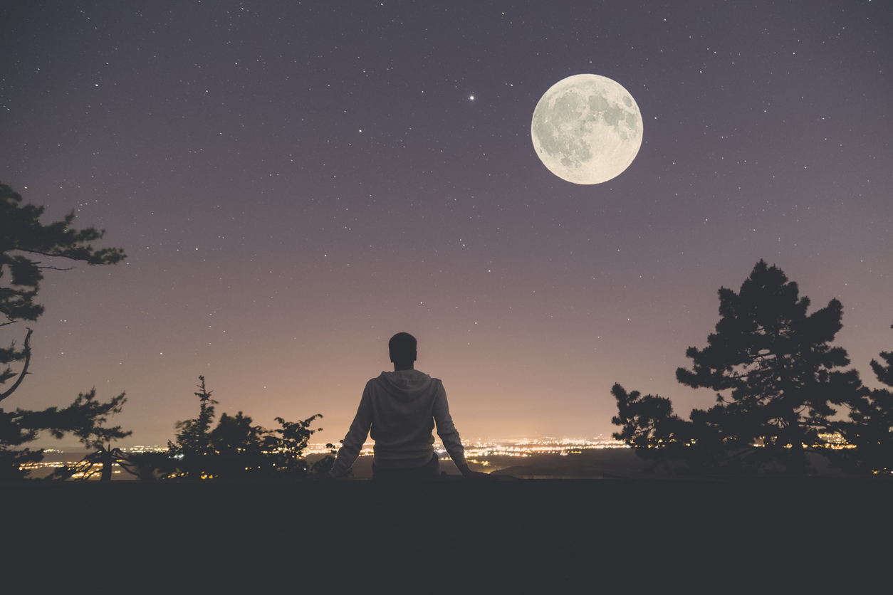 A person looking at a full moon over a city