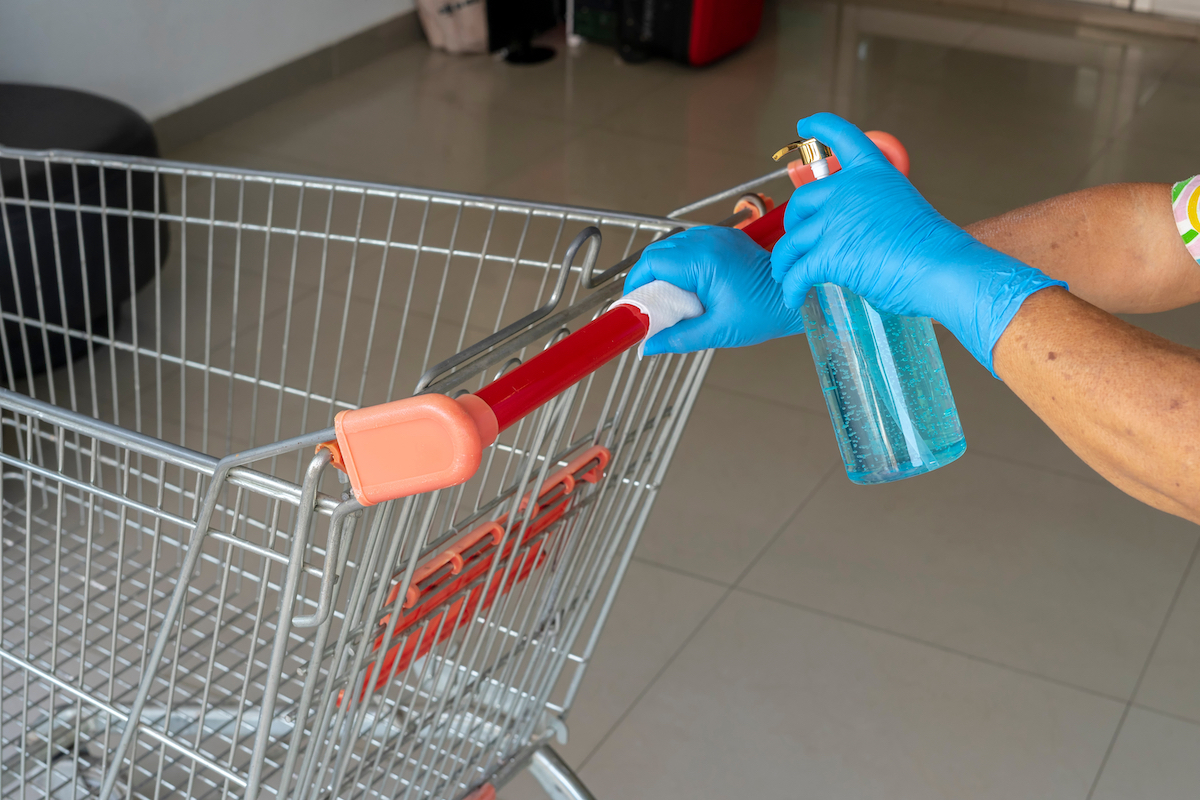 Female Staff disinfecting shopping cart by spraying a blue sanitizer from the bottle on wet wipe.