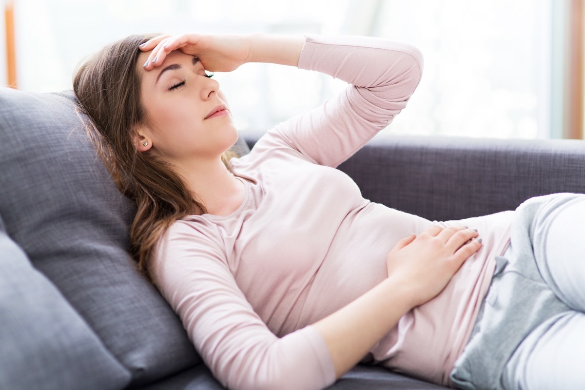 Womach stomachache holding head headache lying down sleeping on couch