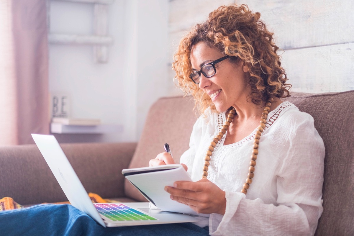 middle age woman working at home with laptop and notebook. writing a note