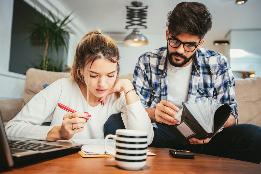 A young man and woman sit on the couch while going over forms to file taxes