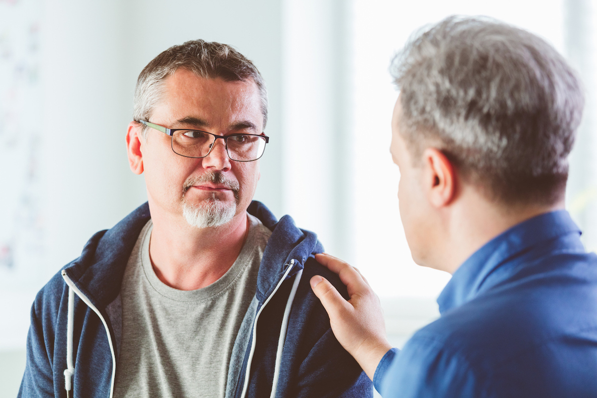 Man comforts friend or partner by putting hand on his shoulder