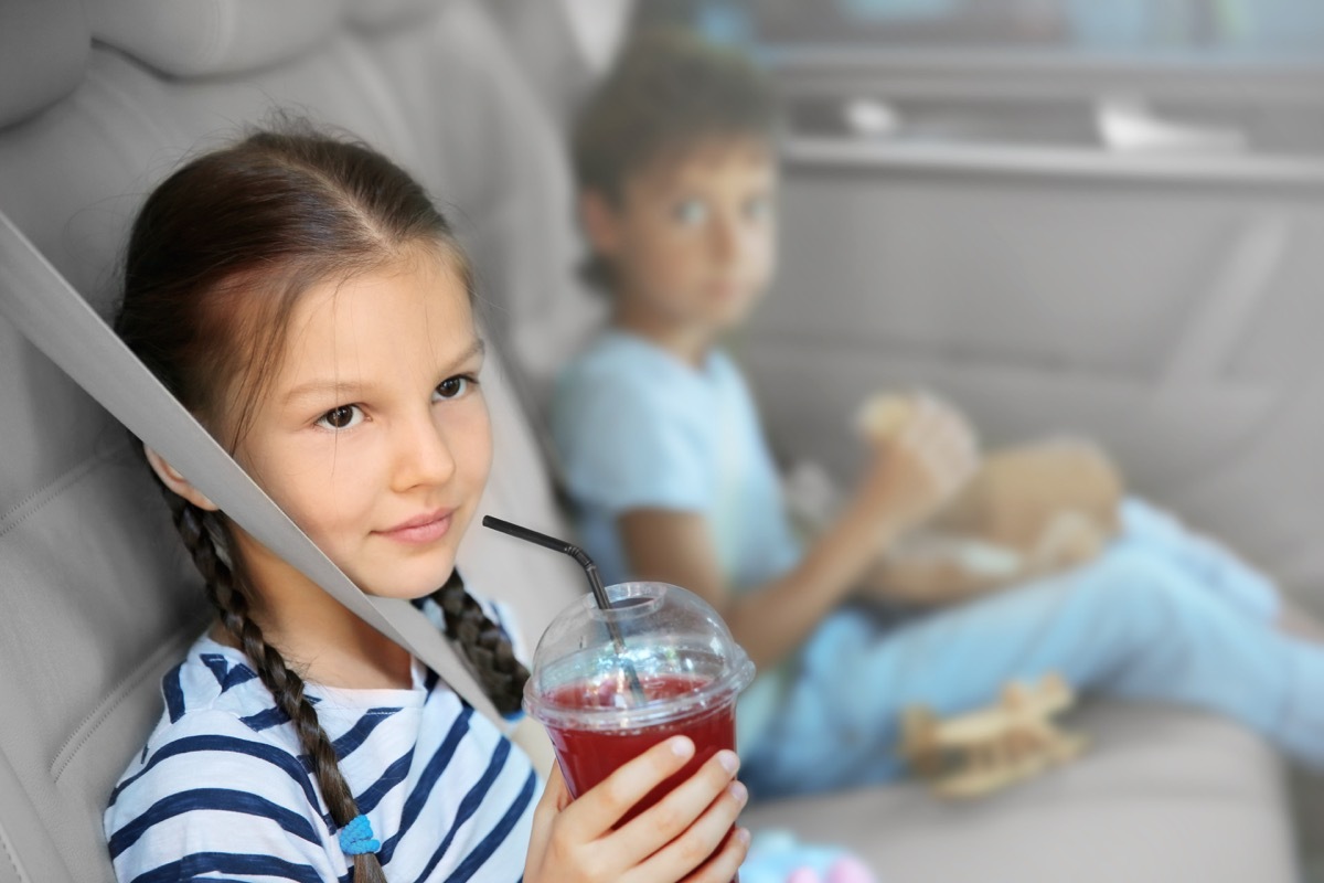 little girl drinking juice in the back seat of a car while her brother eats lunch