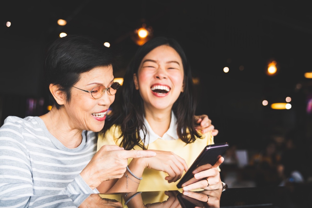 asian mother and daughter looking at a phone screen together, laughing in a cafe