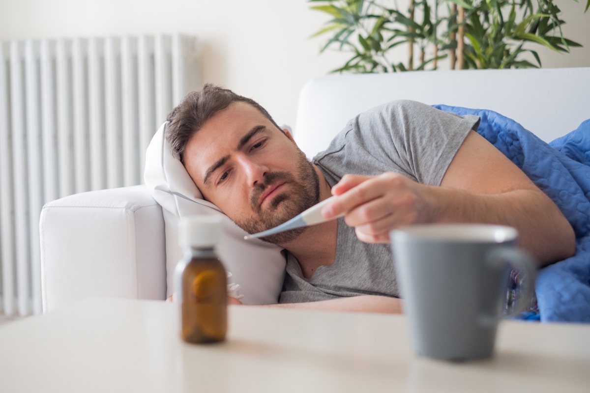 Sick man checking temperature and feeling bad at home