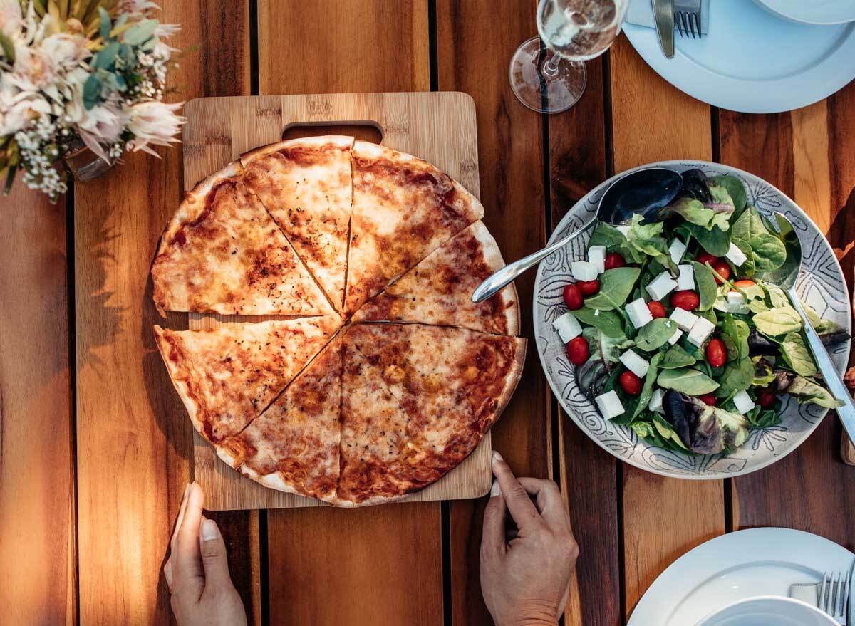 Serving pizza on table with side spinach salad