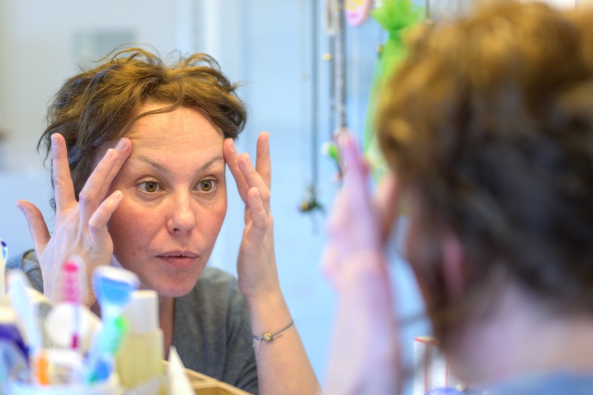 woman checking out her face in a mirror during her morning with a view to her reflection in the mirror