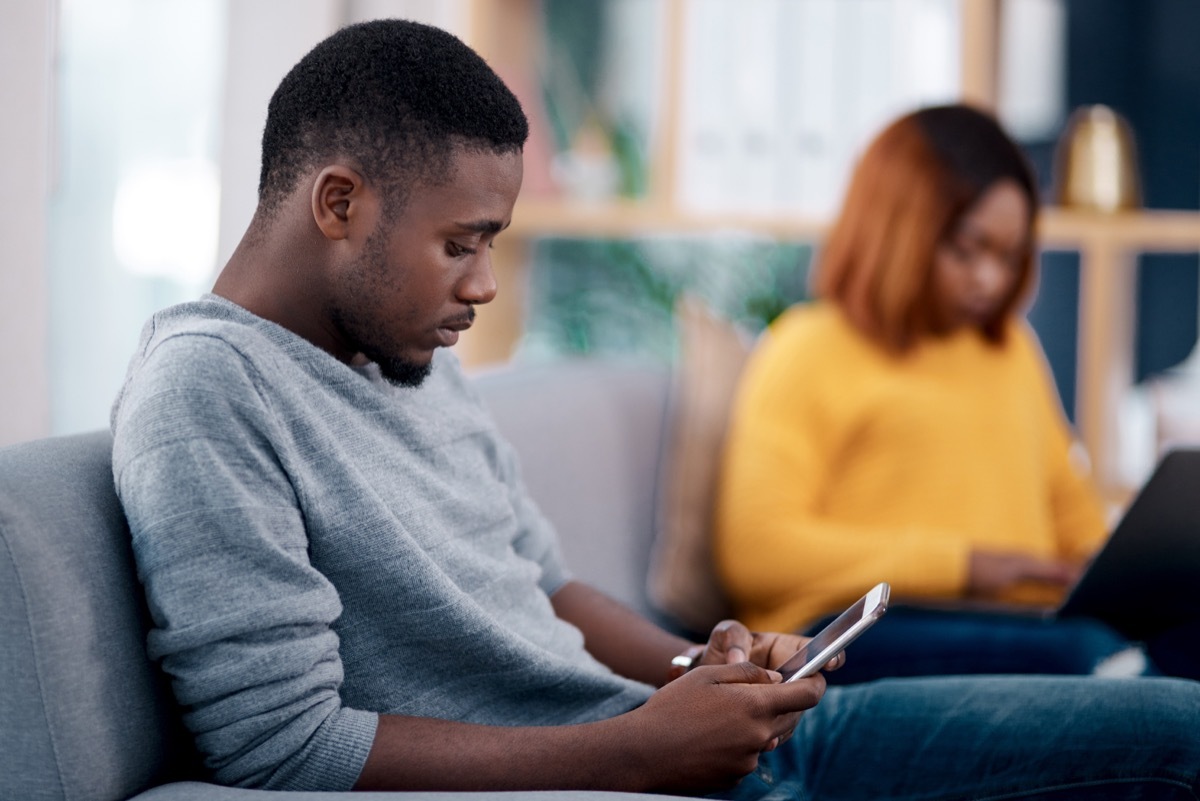 Shot of a young man using his cellphone while his girlfriend sits in the background