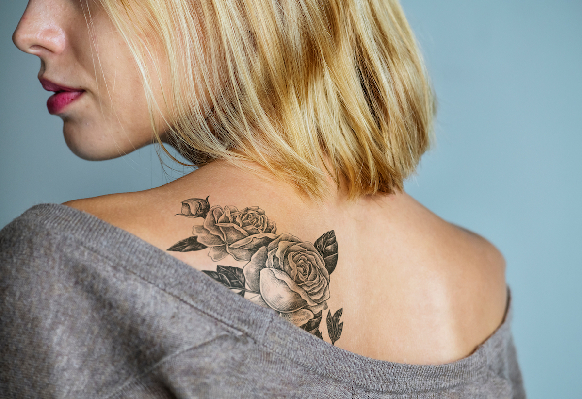 Close up of a young blonde woman's back with a large rose tattoo.