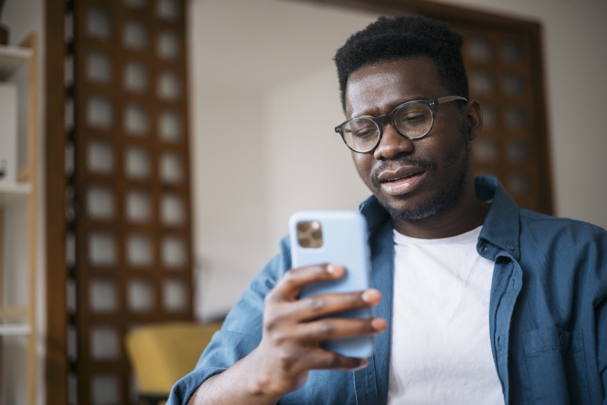 Young man sitting at home, feeling depressed and trying to contemplate bad news he is reading online using a smart phone