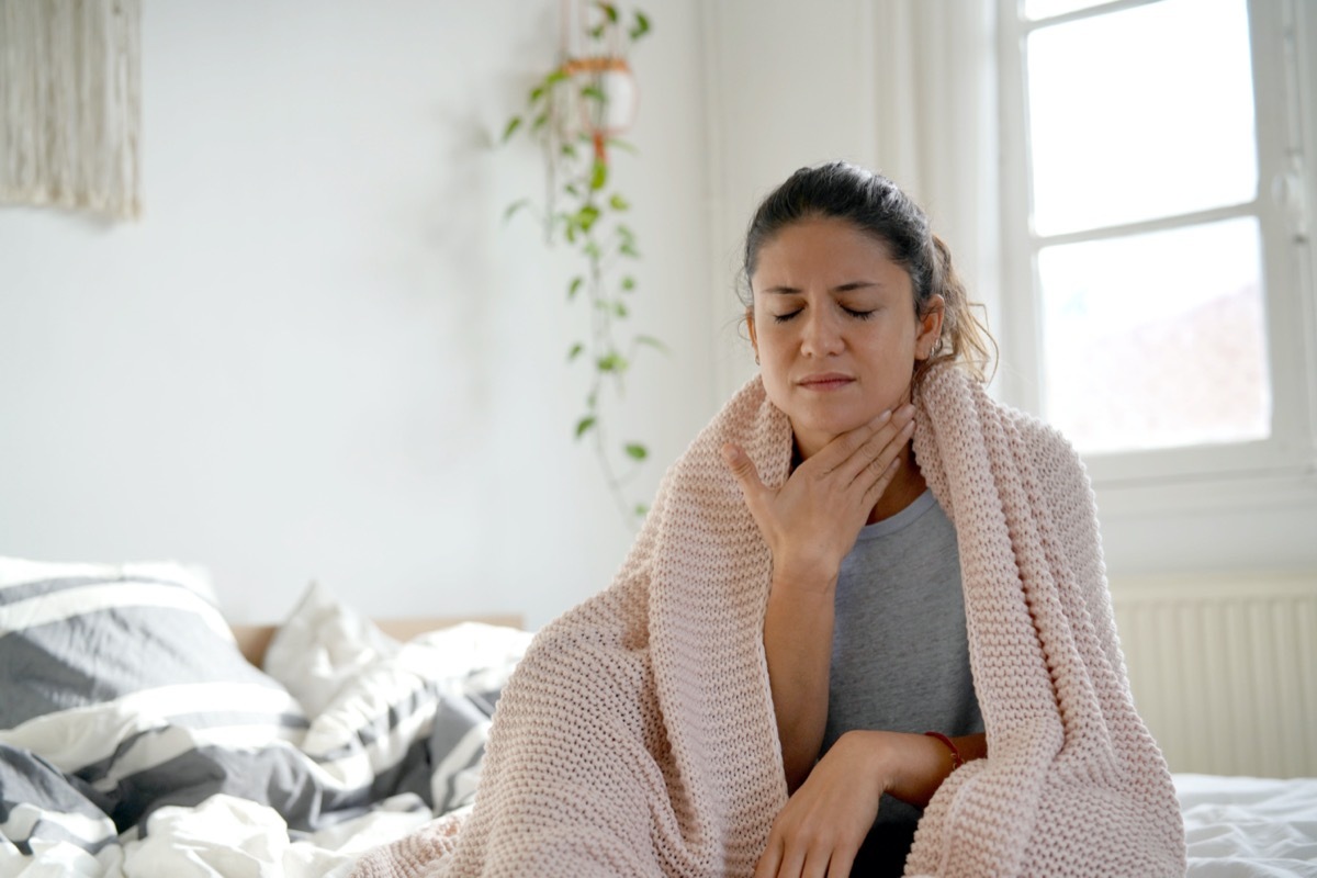 brunette sitting on bed with sore throat