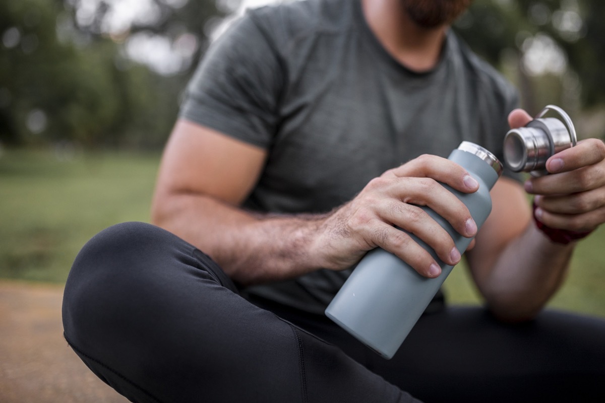 Close up of a reusable water bottle in a human hand, concept of thirst, rehydration and decreasing single use plastic