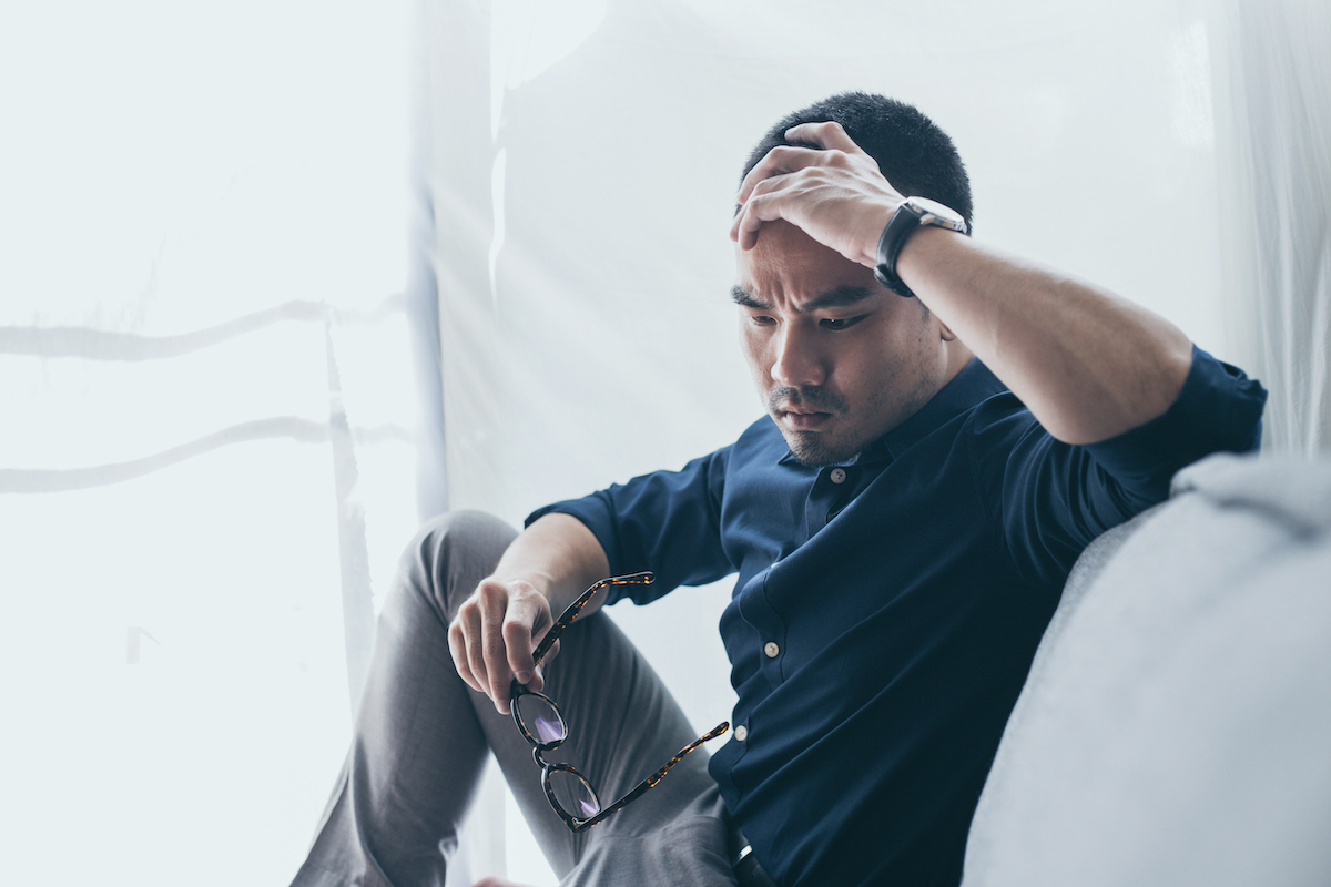 A young man sitting and holding his head looking upset.