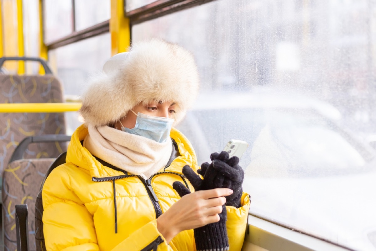 woman in winter clothing with face mask on a bus looking at her phone