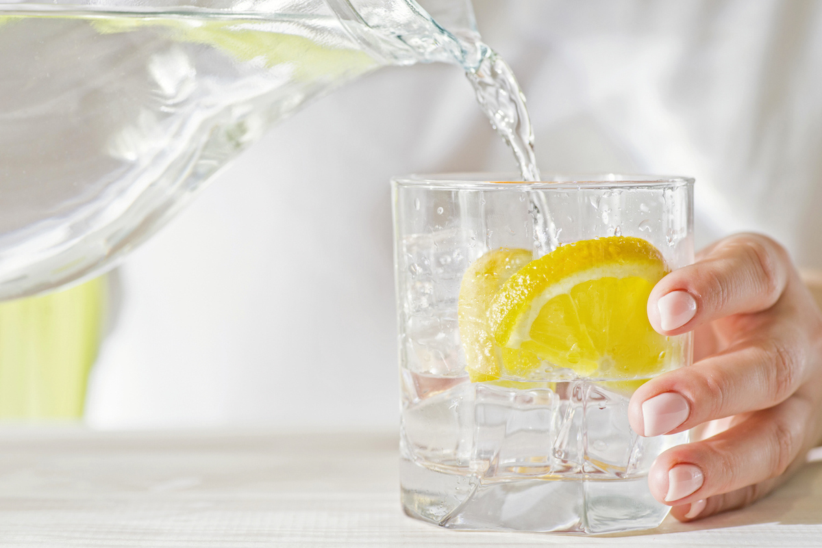 Female hands pouring water from the decanter into a glass beaker with lemon and ice.