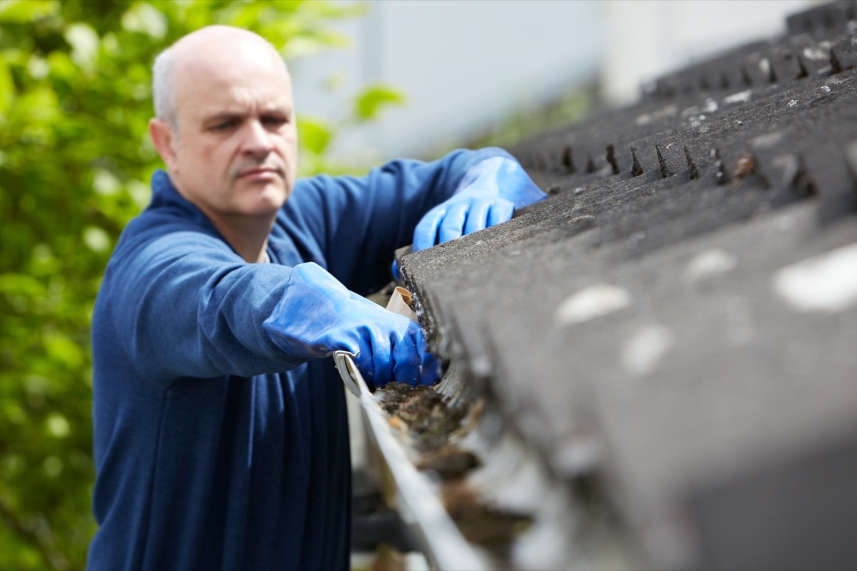 middle aged white man clearing leaves from gutter