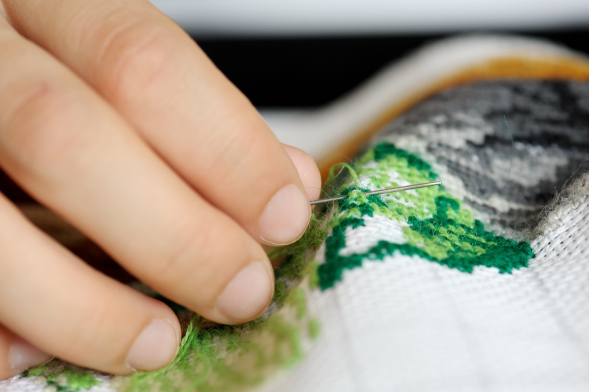 Hands of the girl working upon the embroidery, located on a black background