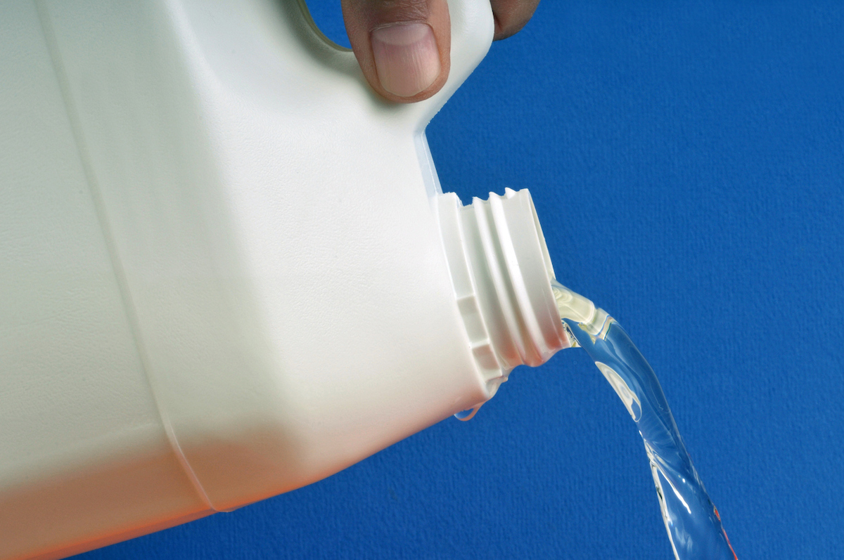 bleach being poured out of white bottle against blue background