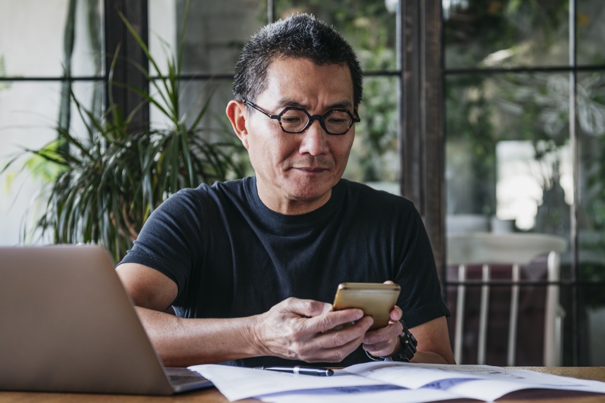 Asian man in his 50s working remotely, using mobile phone, communication, connections, technology