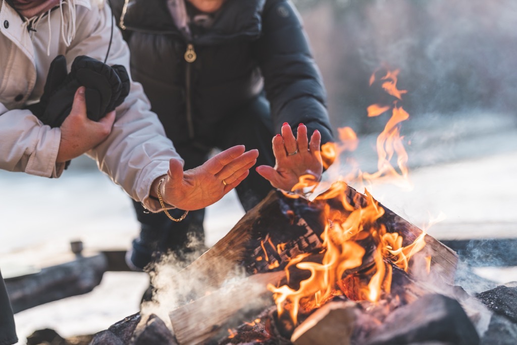 A couple of active senior women are warming up by a campfire on a beautiful sunny winter day in Sweden.