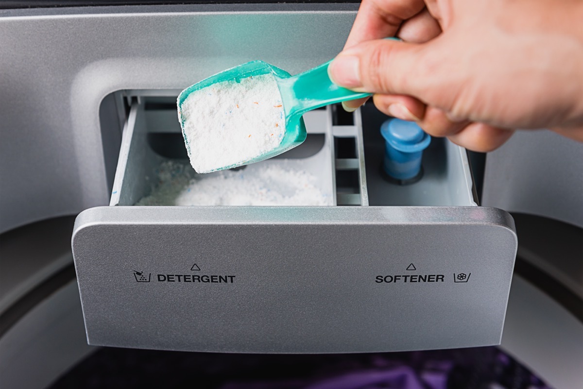 white hand putting powder detergent in washing machine