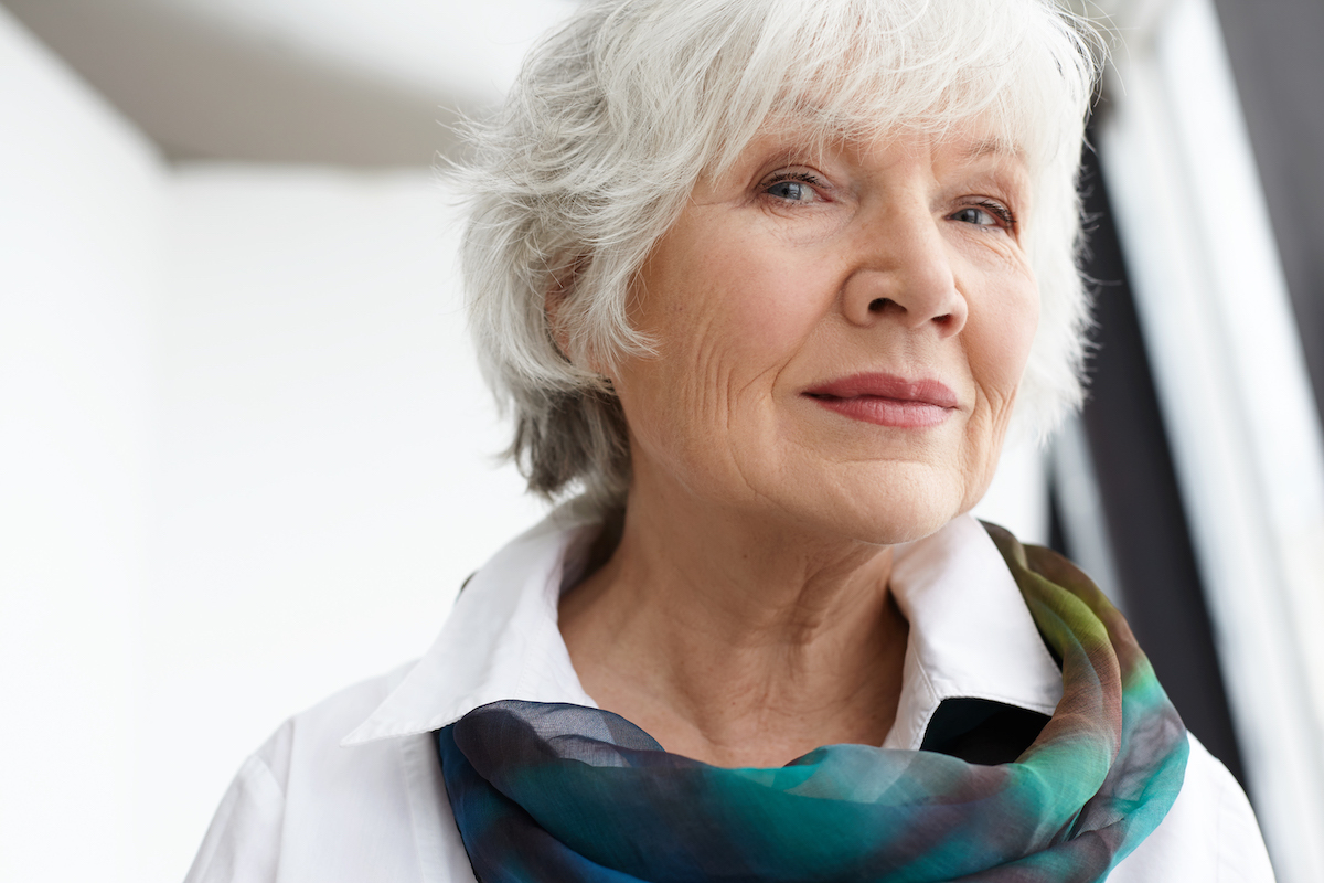 Age, maturity, beauty, style and fashion concept. Close up image of classy stylish senior mature woman with wrinkles, gray hair and natural make up spending leisure time indoors, smiling at camera