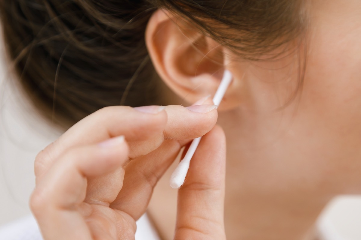 Woman is cleaning ear with a cotton swab