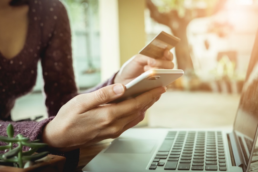 woman sitting in front of a laptop using a credit card to buy something on her smartphone