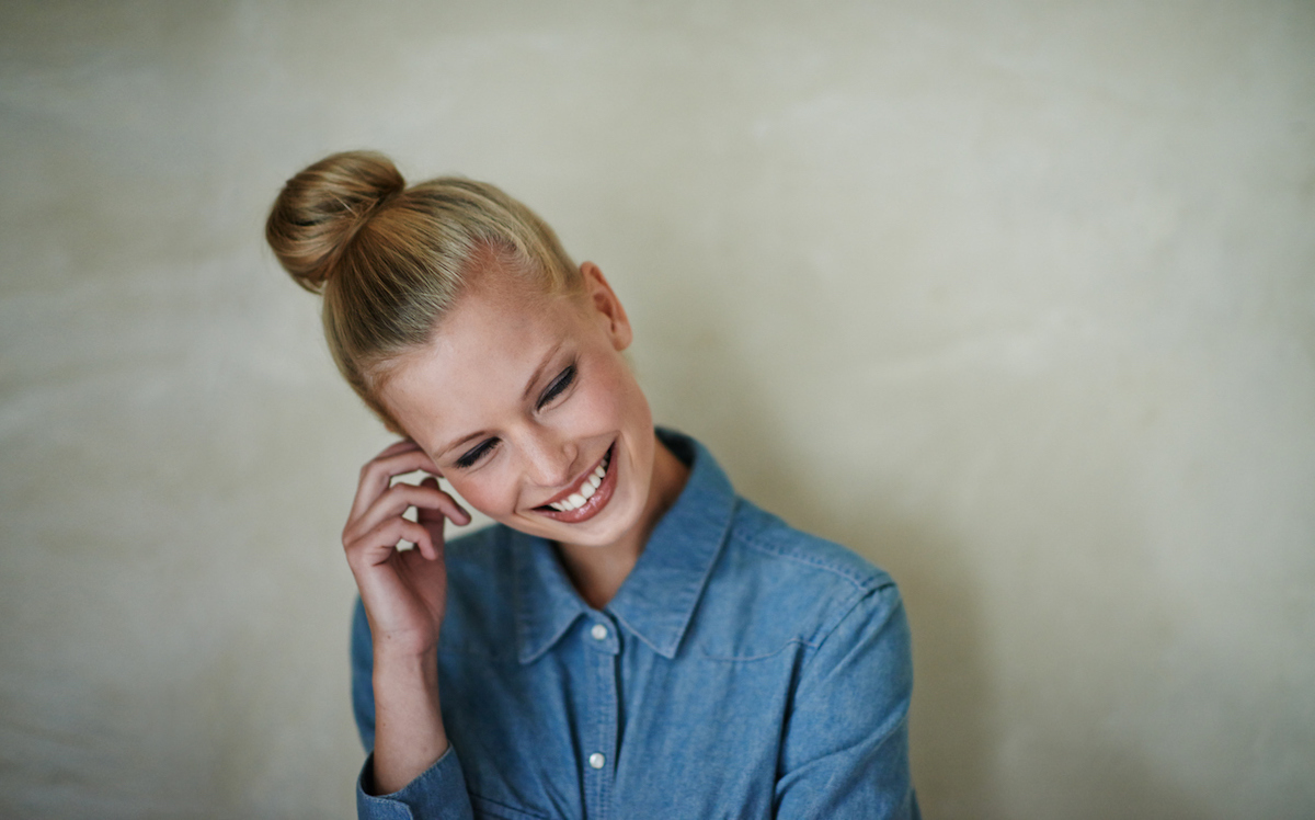 A smiling blonde woman with her hair in a high bun wearing a button-down denim shirt.