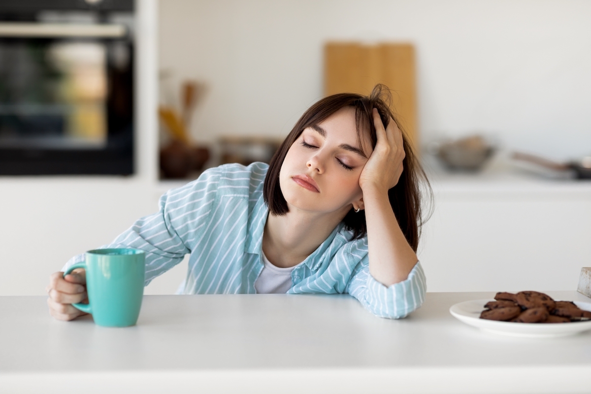 Sleepy young woman drinking coffee at kitchen counter