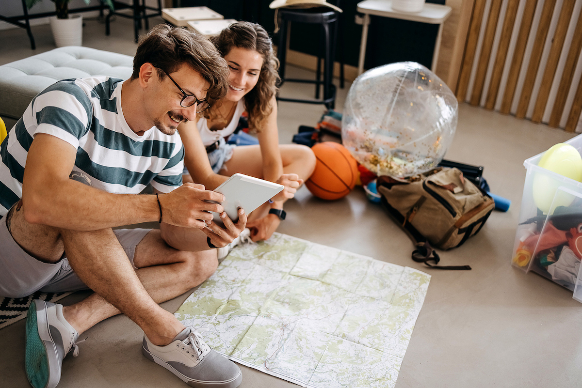 Man and woman planning a vacation trip sitting on the floor looking at a map and a tablet