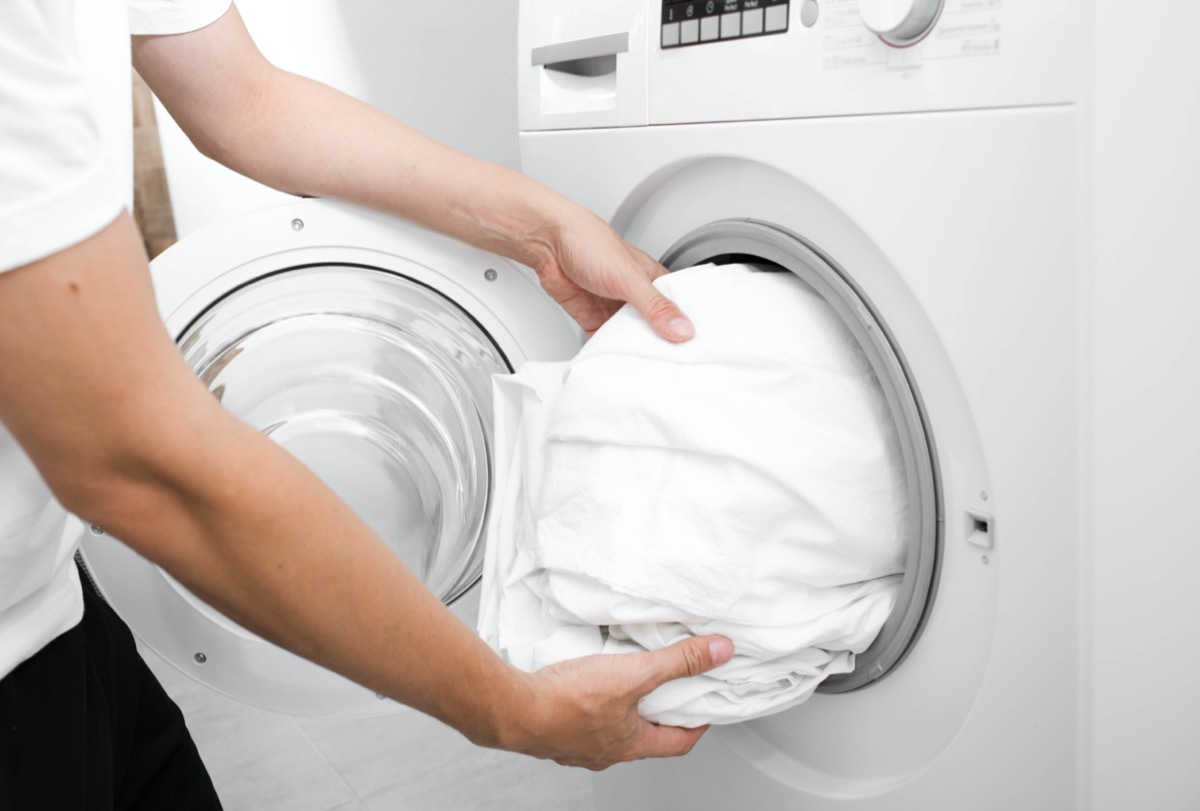 male hand putting a cloth into washing machine. Wash Linen Bedding