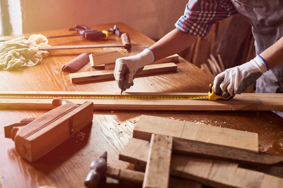 Female craftsmen use tape measure to assemble wooden pieces. Professional carpenter at work measuring wooden planks.