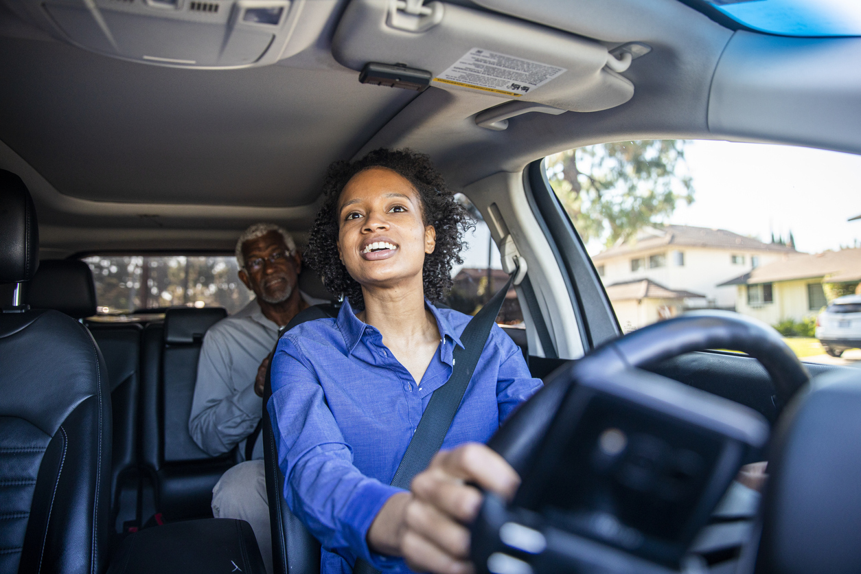 A woman driving a rideshare car with a passenger in the back seat