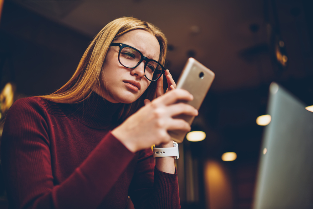 A young woman looking at her smartphone with a confused or concerned look on her face