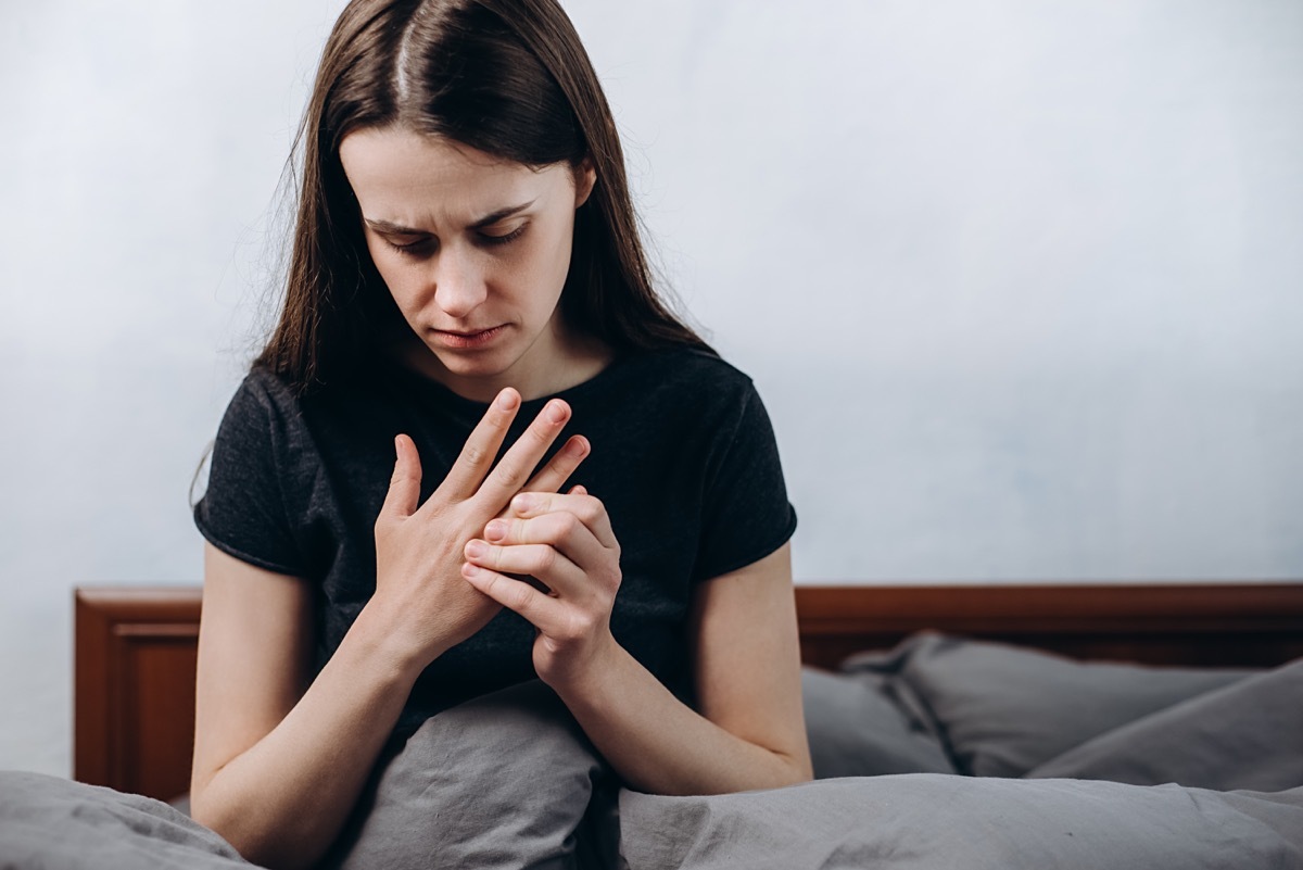 Close up of sad tired woman suffering from pain in hand or wrist sitting on bed at home, girl patient touching wrist feeling hurt joint pain having osteoarthritis disease health problem