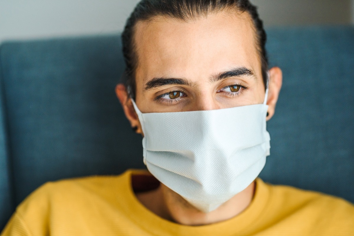 Young man wearing a protective medical face mask and feeling apathetic. Indoor photo. Coronavirus protection / staying at home during quarantine concept.