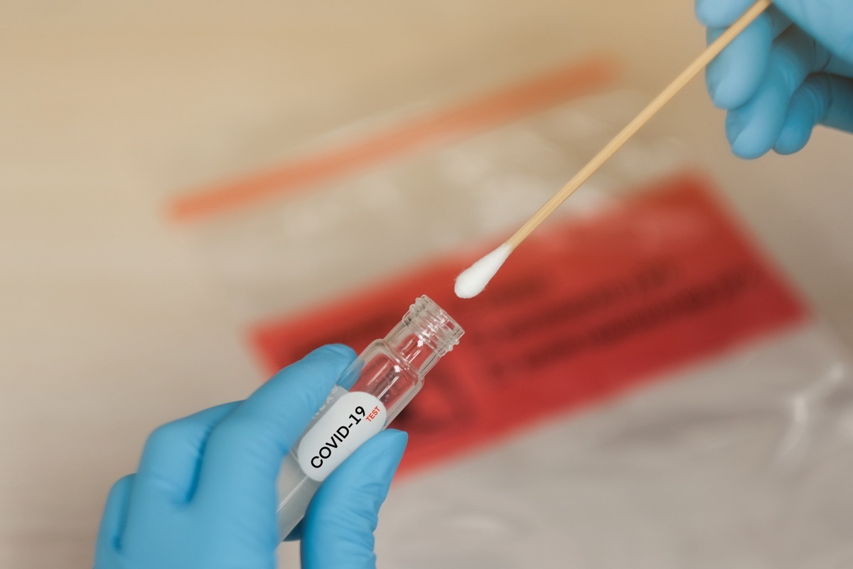 gloved hands in lab putting a swab into coronavirus test vial