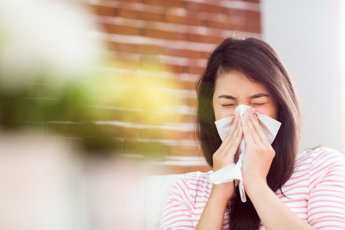 Asian woman blowing her nose on couch at home in the living room