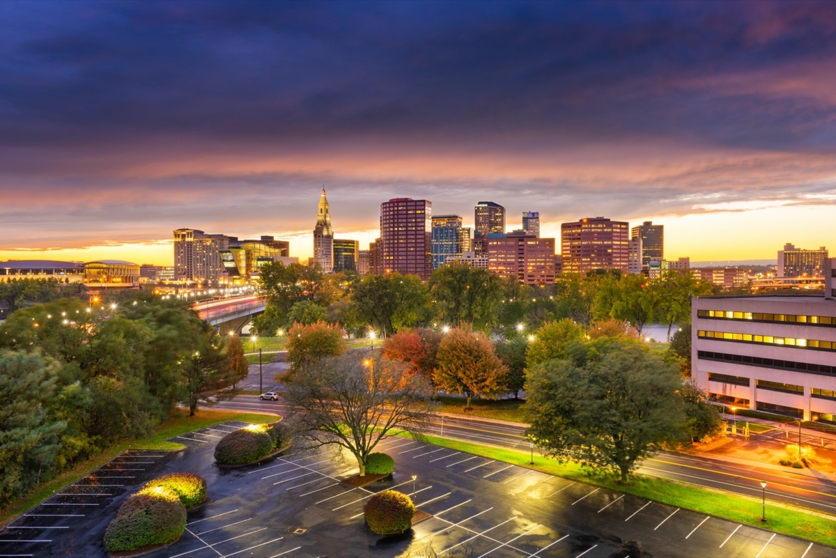 cityscape photo of an empt parking lot, trees, buildings, and a busy highway in Hartford, Connecticut at sunset