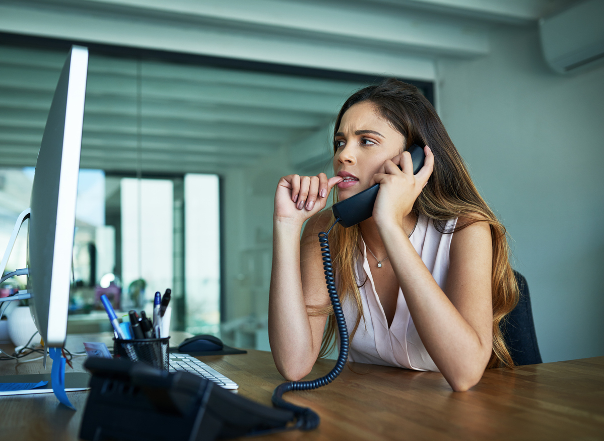 woman biting her nails while on the phone in front of a computer