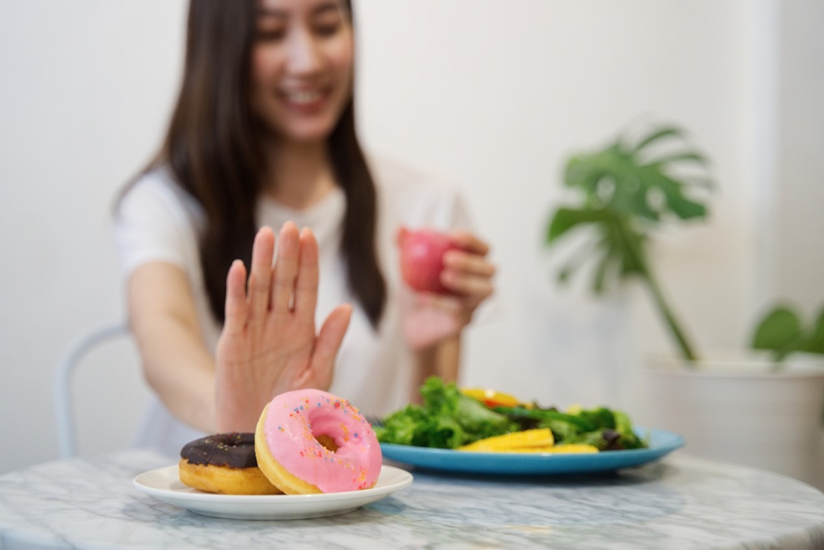 young asian woman with a plate of salad in front of her pushing away a plate of donuts