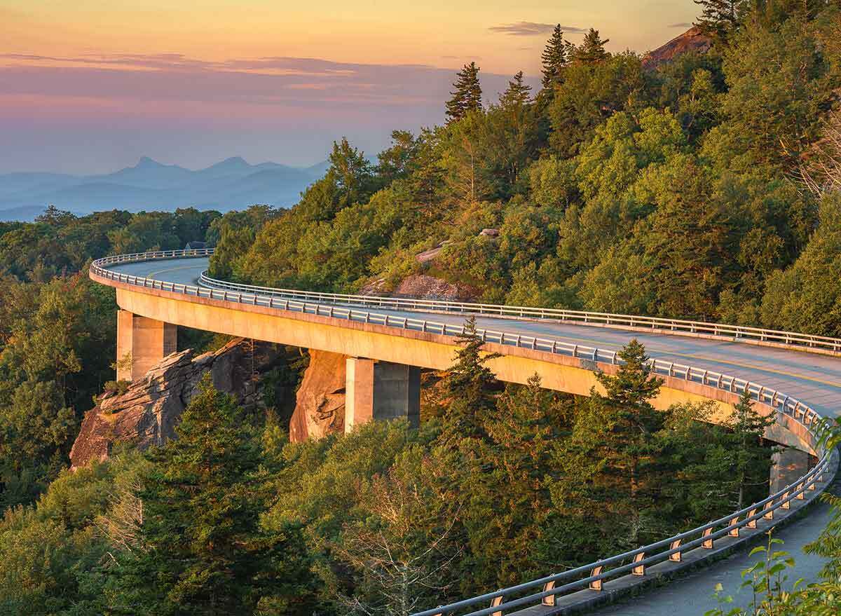 a winding road curves around a forested cliff