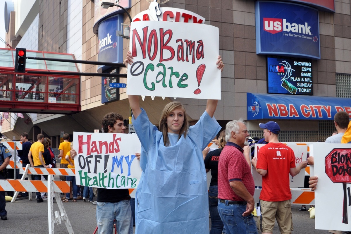 Young woman in hospital gown holds up 