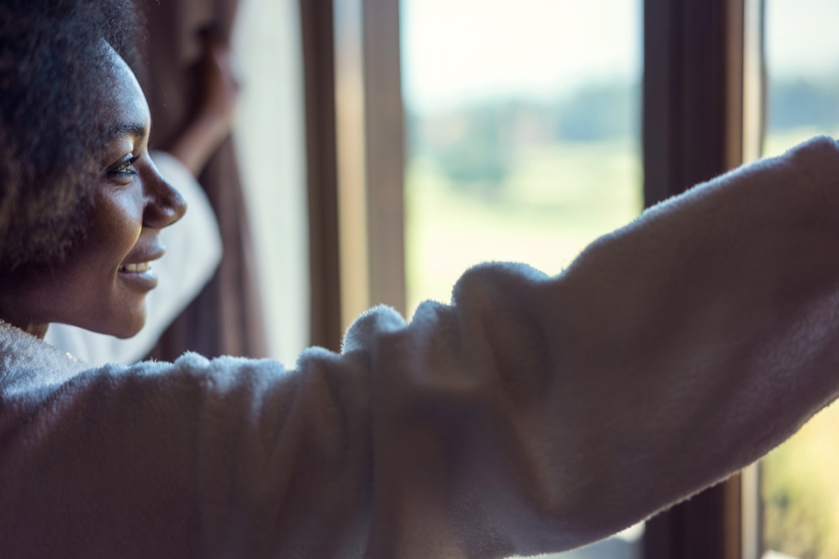 young black woman looking out the window and smiling in the morning