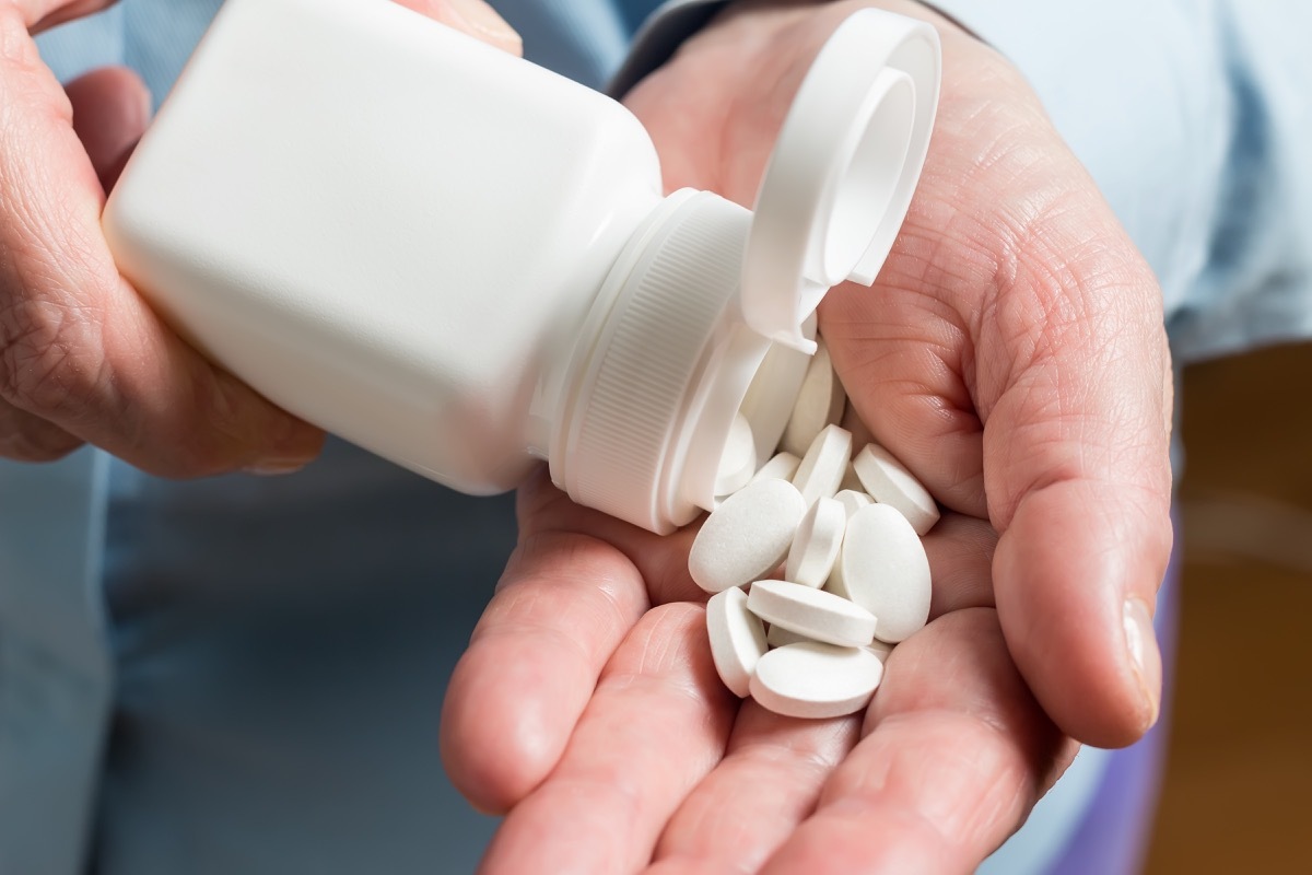 Woman hand holds white medication pills, pours from a white bottle into palm the calcium tablets dietary supplement.