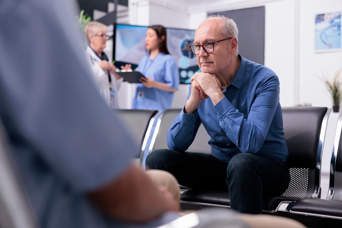 Stressed tired senior patient sitting on chair in hospital lobby while waiting for specialist doctor to start medical examination during checkup visit consultation. 